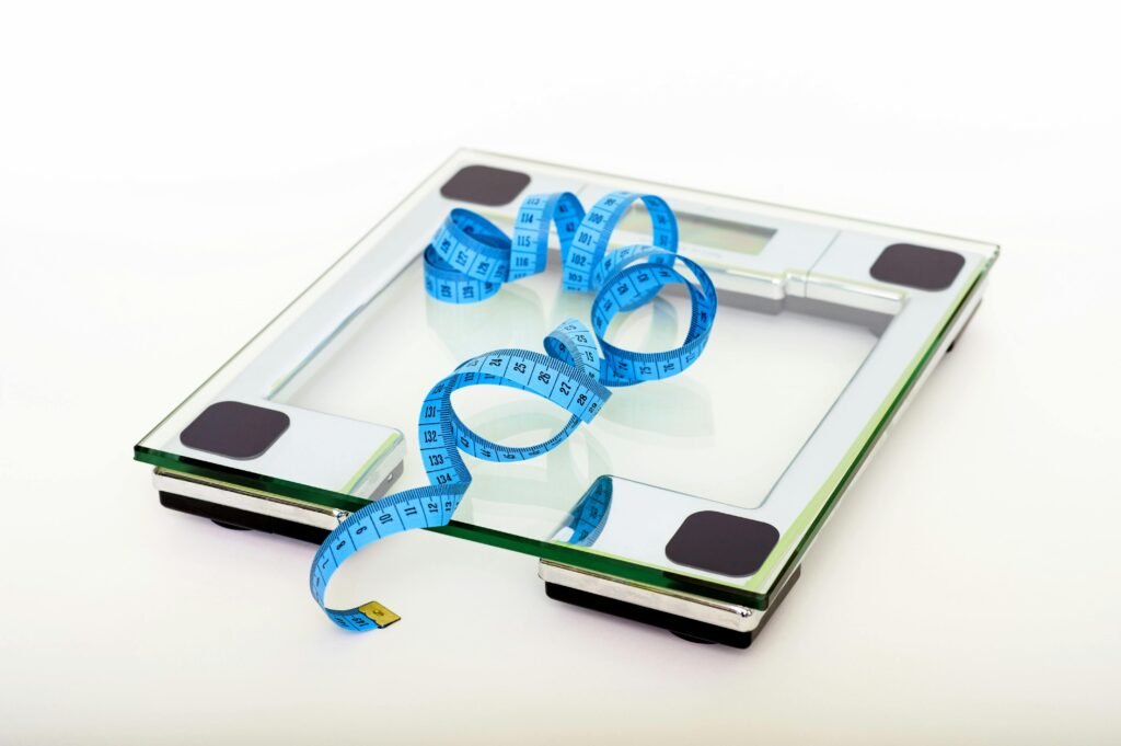 A digital glass weighing scale with a blue measuring tape, symbolizing weight management. weight tracking.