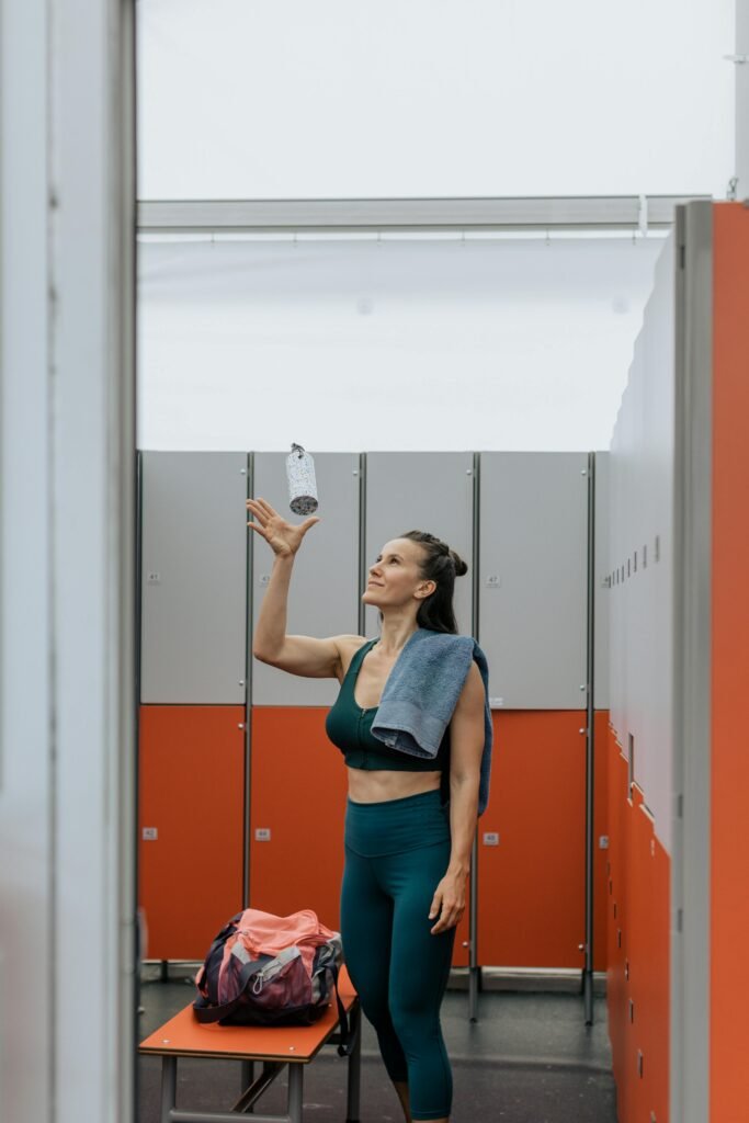 Woman in gym changing room with a towel and water bottle, preparing for fitness training.