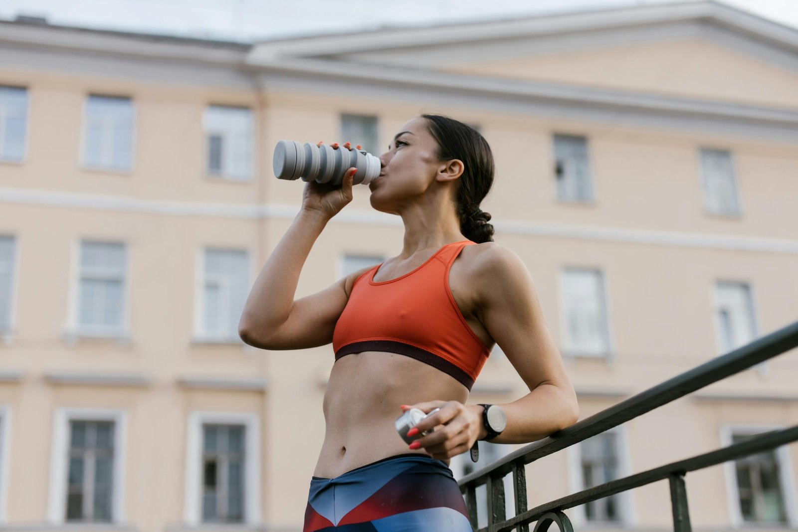 Athletic woman in sportswear hydrating with water bottle outdoors in urban setting.
