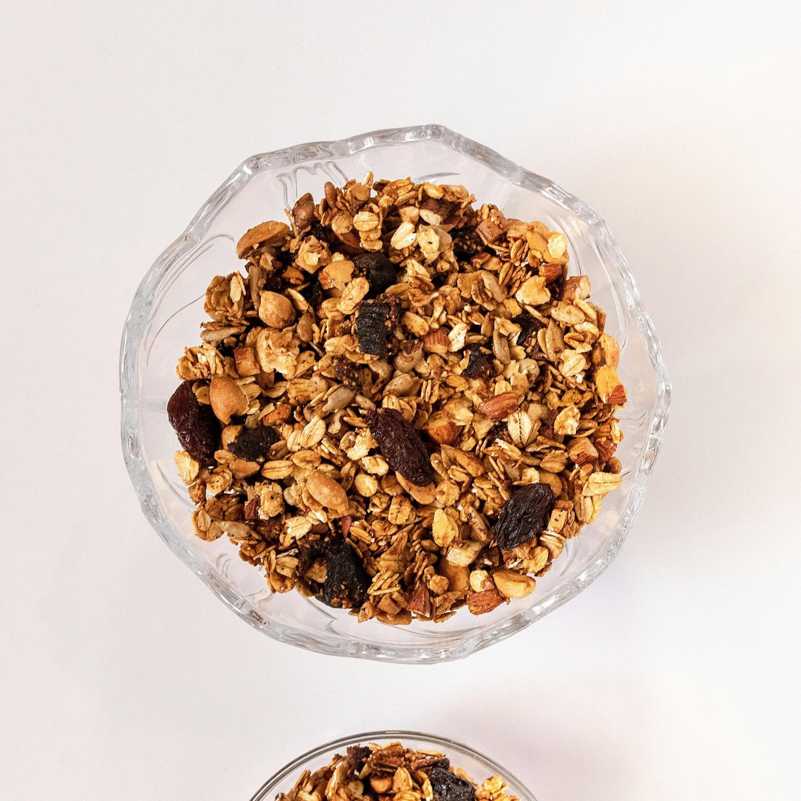 Top view of two bowls of nutritious granola with nuts and dried fruits on a white background.
