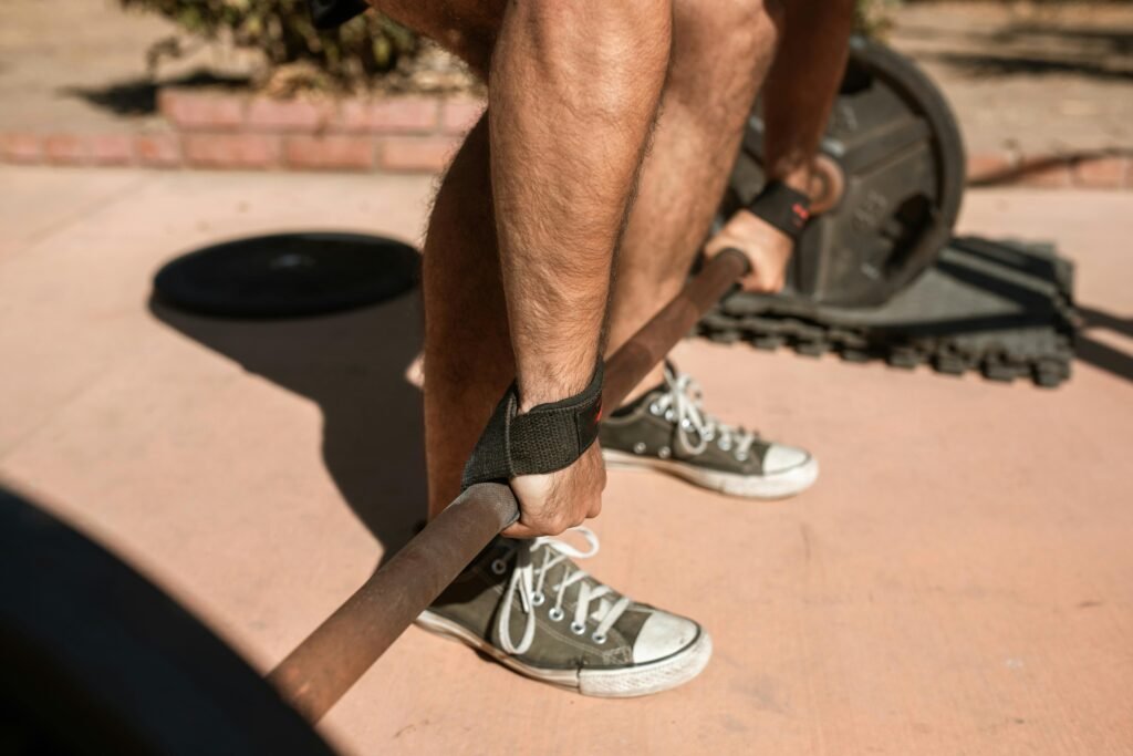 Close-up of a man lifting weights outdoors wearing casual sneakers on a sunny day.