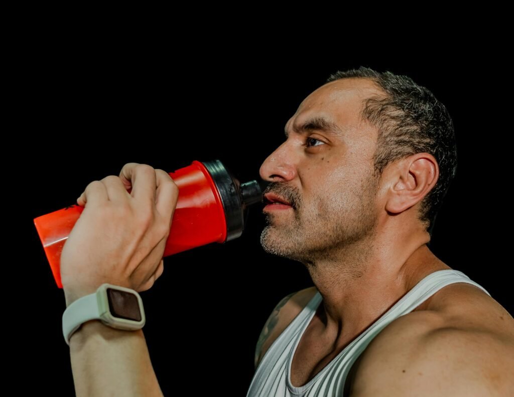 Fit adult male drinking from shaker bottle, fitness focus, black background.