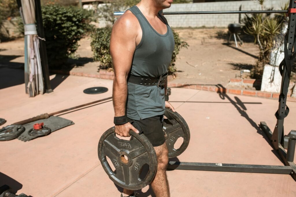 Man lifting heavy weights in an outdoor gym setting under bright sunlight. A Guide To The Best Weightlifting Belts: Which Weight Lifting Belt Should I Buy (May 2025 Rankings)