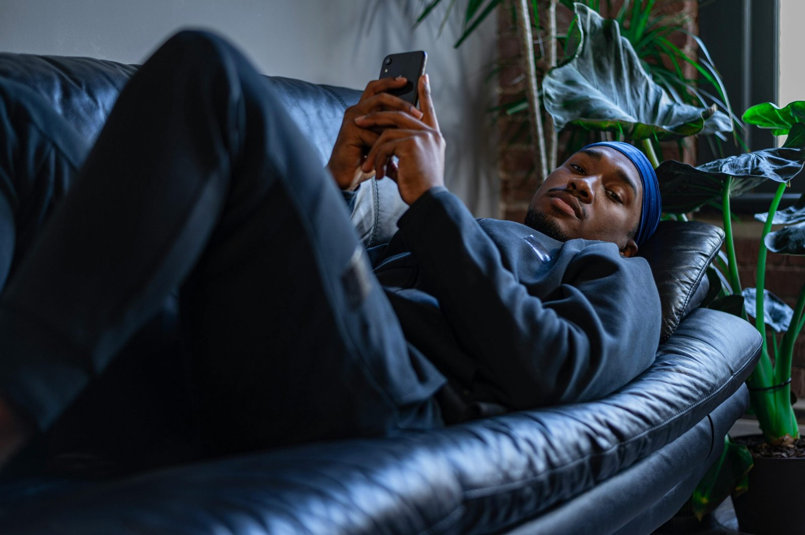 A man lying on a sofa in a comfortable indoor setting, using a smartphone.