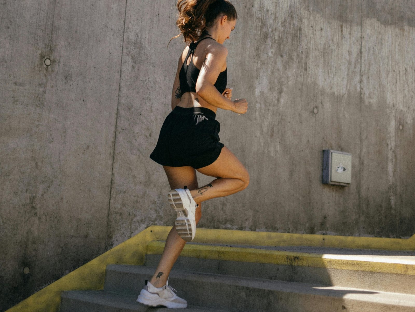 Athletic young woman in activewear running on outdoor concrete stairs, showcasing fitness and strength.