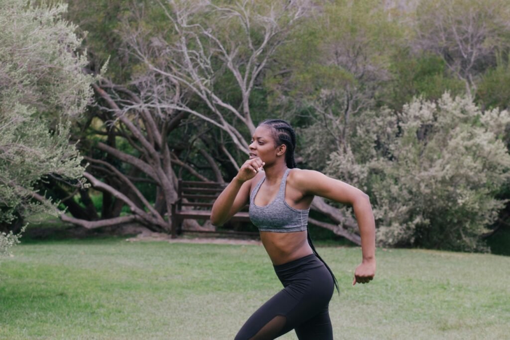 Fit black woman jogging outdoors, embracing fitness and health in a lush park environment.