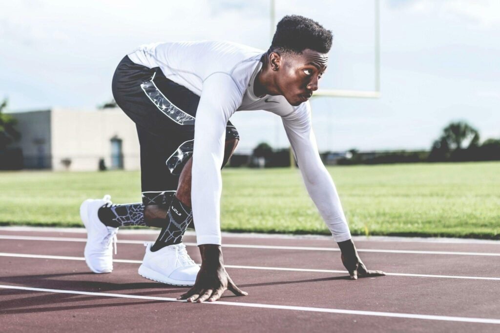 Focused athlete in starting position on a sunny track field, ready to sprint. Best Men's Compression Shirts for Weightlifting and Recovery (2025)