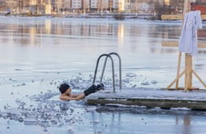 Man in icy water near a wooden dock with towel in the winter landscape.