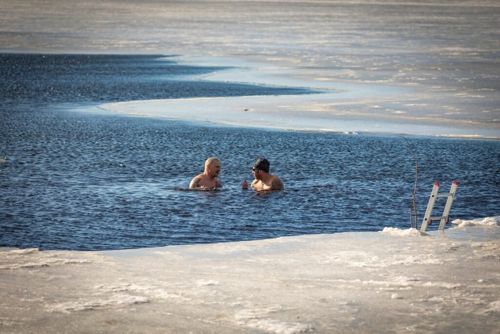 Two men brave the cold for a swim in a partially frozen lake during winter.