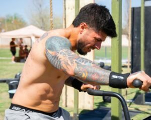 Focused male athlete with tattoos working out on an assault bike outdoors.