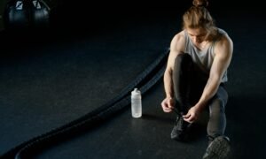 Man tying shoes on gym floor with battle ropes and water bottle, ready for training.