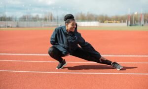 A woman in activewear stretches on a red running track outdoors, preparing for a workout.