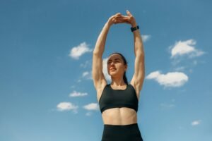 Woman in sports bra stretching under a clear blue sky, embodying fitness and wellness.