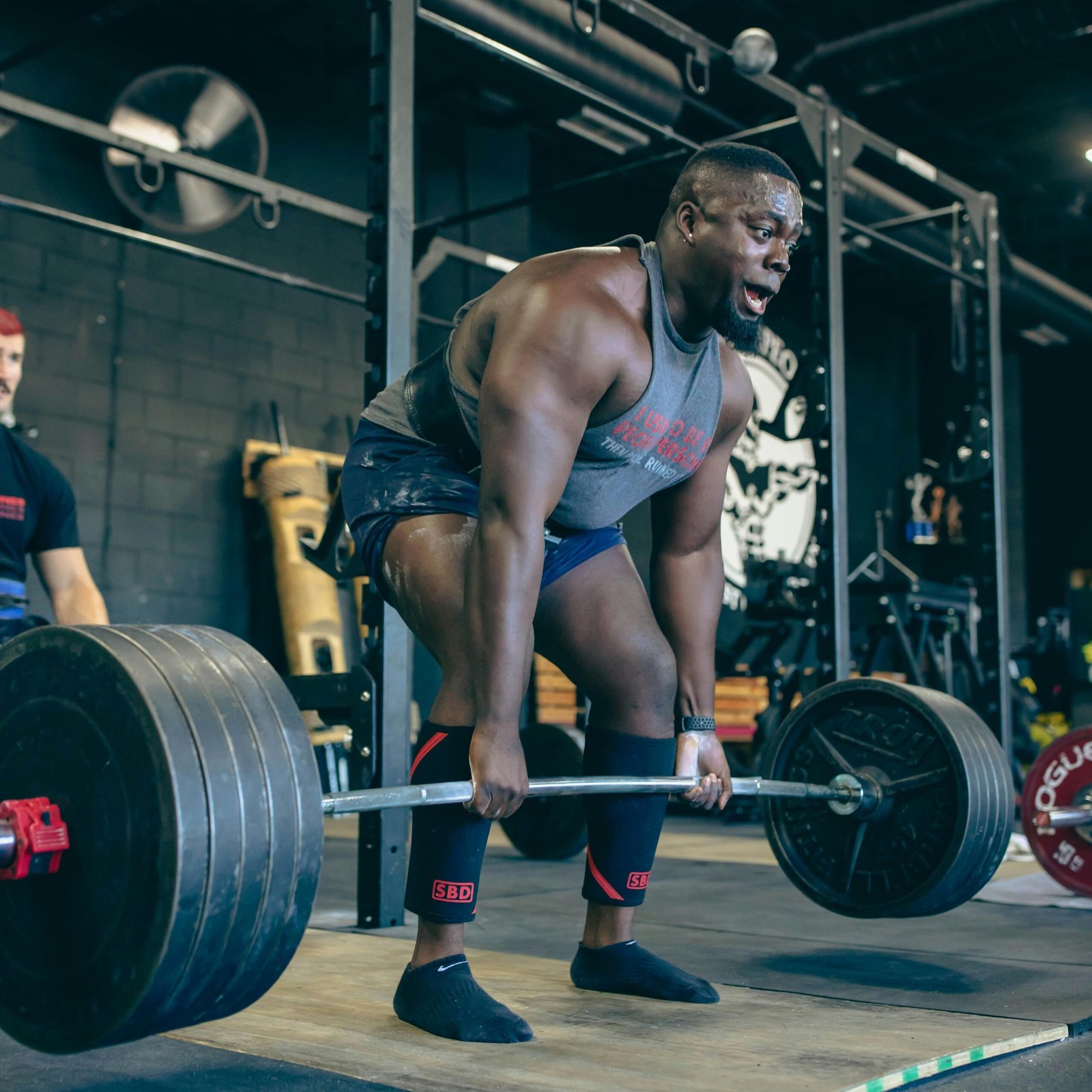 A muscular man performs a heavy deadlift in a gym, showcasing strength and fitness.