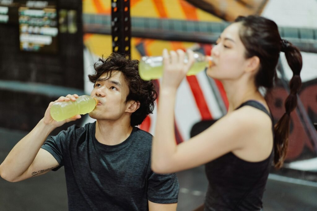 Fit Asian couple hydrating at the gym after an intense workout. Refreshing drink break.